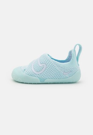 Vaaleansininen neulotun kuvion slip-on-kengät, joissa on kumipohja, suurella valkoisella logolla sivulla ja pienellä vetotapilla kantapäässä helppoa pukemista varten.