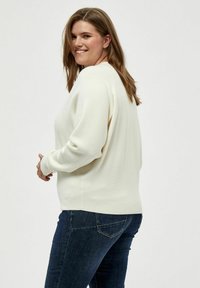Weißer Pullover mit langen Ärmeln, gerippten Bündchen und Saum, kombiniert mit dunkelblauer Jeans. Der Pullover hat eine lockere Passform und eine glatte Textur.