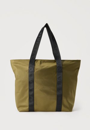 Bolso tote verde oliva con asas negras y el logotipo "ARKK" en relieve repetido en las correas, colocado verticalmente sobre un fondo blanco.
