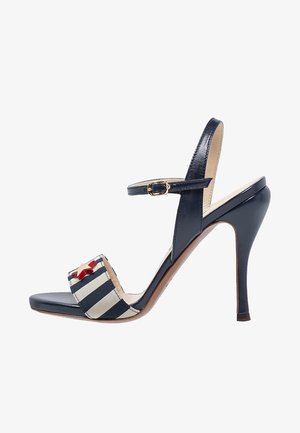 Granatowa sandał na wysokim obcasie o błyszczącej powierzchni, z paskiem z materiału w paski i czerwonym akcentem w kształcie gwiazdy. Regulowany pasek na kostkę dla lepszego dopasowania.