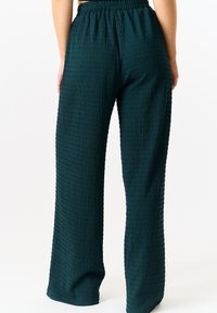 Green textured wide-leg pants with an elastic waist, featuring a rippled pattern. Fabric appears lightweight with a relaxed fit.