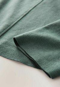 Tissu tricoté vert doux en gros plan montrant une manche pliée et des détails de couture visibles.