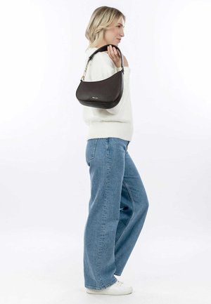 Borsa a spalla in pelle marrone con una superficie liscia e dettagli in oro, portata da una persona che indossa un maglione bianco e jeans blu.