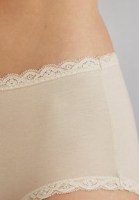 Světlé béžové boyshorts s jemným krajkovým lemem na pase, měkkou Texturou a hladkým materiálem.