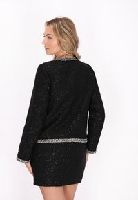 Compleu format din jachetă și fustă din tweed negru, cu detalii din argint, având un finisaj texturat, mâneci lungi și un guler rotund.