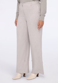 Vaaleanharmaat leveälahkeiset housut, joissa on teksturoitu pinta, sujuva vyötärönauha ja nappikoristeet lahkeissa, yhdistettynä kremaisiin korkovalopohjaisiin kenkiin.