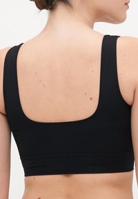 Bra sportivo nero con spalline larghe, schiena a sco scoop e un materiale liscio ed elastico dal design elegante e minimalista.