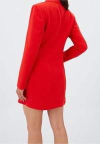 Rode blazerjurk met lange mouwen, getailleerde pasvorm en een reverskraag. Gladde stof met minimale naden en geen zichtbare hardware of versieringen.