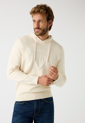 Felpa crema con un logo "GUESS" goffrato e testurizzato in un design triangolare. Presenta un cappuccio regolabile con cordini e polsini e orlo a costine.