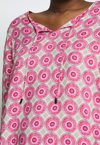 Haut léger avec un motif floral circulaire rose et beige, encolure en V et détails à cordon, fabriqué en tissu respirant.