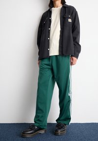 Black denim button-up shirt, cream t-shirt, green track pants with white stripes, and black shoes with a thick sole.
