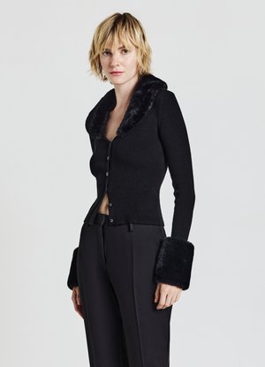 Cardigan nero a coste con colletto in pelliccia sintetica. Presenta bottoni aderenti e ampi polsini in pelliccia sintetica. Abbinato a pantaloni neri.