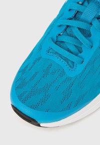 Lichtgewicht sportschoen met een ademend turquoise mesh bovenwerk met gestructureerde patronen, platte veters en een zwart-witte rubberen zool.