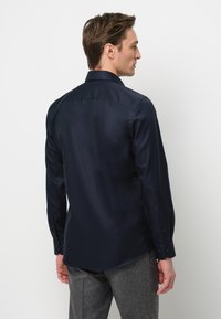 Marineblauw overhemd met lange mouwen, een geklede kraag en een gladde textuur, gecombineerd met grijze broeken.