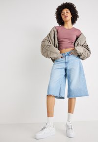 Heledad helesinist sinine teksapüksega, millel on toore äär, sobitatud kinnise mauve'i topiga ja polsterdatud oliivroheline bomber-jakk. Valged spordijalatsid täiustavad välimust.