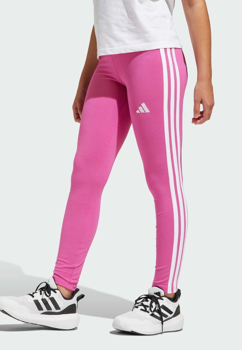 Leggings rosa con tre strisce bianche sui lati, caratterizzati da un logo Adidas sulla coscia sinistra. Il materiale sembra liscio e elastico.