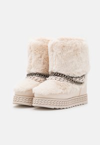 Botines de tobillo de piel sintética crema con tacones de cuña, con una textura trenzada y un adorno de cadena alrededor de la entresuela. Suela de goma que proporciona agarre.