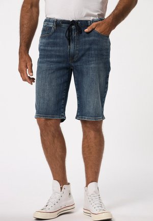 Mørkeblå denimshorts med snor i taljen. Har opkrøllede kanter, forlommer og en afslappet pasform. Bæres med hvide høje sneakers.