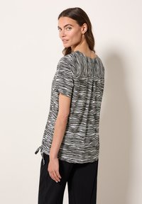 Maglietta a strisce zebrate bianco e nero con maniche corte, scollatura rotonda, dettaglio di piega sul retro e lacci laterali per una vestibilità regolabile.