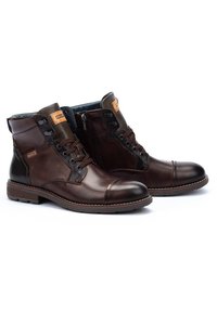 Brown leather ankle boots with a smooth finish, featuring a side zipper, lace-up front, and textured panels. Rubber sole with contrast stitching.