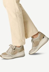 Baskets de sport beiges avec une tige en mesh texturé, des accents en cuir et une semelle blanche surélevée. Dotées d'une fermeture éclair sur le côté et d'un laçage.