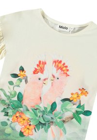 Kratkām piedurknēm krēma t-krekls ar grafiku, kurā attēloti divi rozā kakadi, vidū zaļas lapas un oranžas ziedi, ar ruffles piedurknēm.