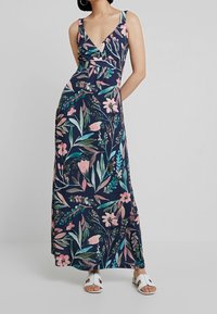 Maxi sukienka w kwiaty w granatowym kolorze, z dekoltem w kształcie litery V, szerokimi ramiączkami i luźnym krojem, z różowymi i zielonymi wzorami kwiatowymi na całej powierzchni.