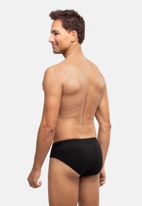 Schwarze Baumwollslips mit einem weichen elastischen Bund, die eine glatte Textur und eine enge Passform aufweisen, von hinten gezeigt.