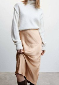 White knit sweater with a high neck paired with a beige satin skirt featuring an asymmetrical hem, complemented by knee-high brown boots.