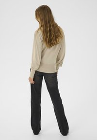 Pull beige à manches longues en tissu texturé, associé à un jean en denim foncé évasé. La tenue met l'accent sur une coupe décontractée.