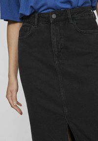 Black denim skirt featuring a straight-cut design, high waist, front slit, and visible stitching, with a button closure and side pocket.
