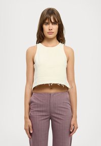 Kortermet cropped topp i blek kremfarge med rå kant, kombinert med lyse lilla bukser med smale striper. Jevn tekstur, enkel design.