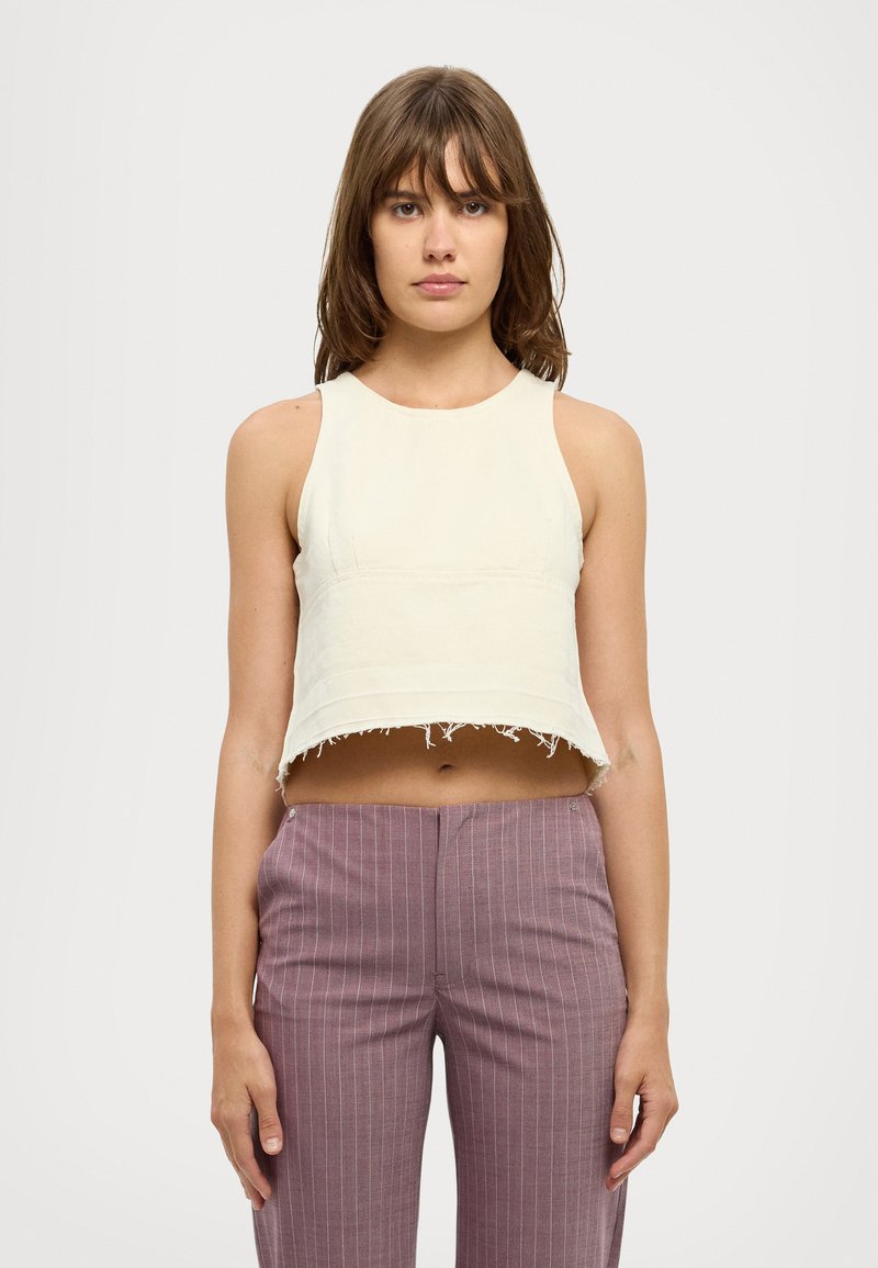 Kortermet cropped topp i blek kremfarge med rå kant, kombinert med lyse lilla bukser med smale striper. Jevn tekstur, enkel design.