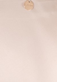 Beige stof met een gladde textuur, voorzien van een cirkelvormig metallic label met het woord "BIZUU" erop. Eenvoudig en minimalistisch ontwerp.