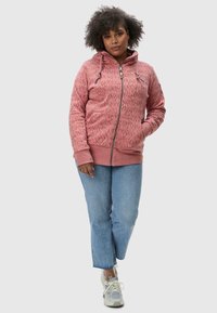 Felpa rosa con zip e motivo testurizzato, con cappuccio regolabile e polsini a coste. Abbinata a jeans azzurri a gamba dritta e sneakers.