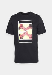 Camiseta de algodón negra con un estampado gráfico de círculos amarillos superpuestos sobre un fondo rosa dentro de un marco rectangular blanco.