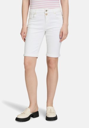 Shorts en denim blanc de style bermuda avec un ourlet roulé, des poches à l'avant et une fermeture à bouton métallique, portés avec des mocassins blancs à semelle noire.