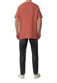 Koszulka krótki rękaw, teksturowana, w kolorze rdzy, o luźnym kroju, połączona z dopasowanymi, wyblakłymi czarnymi dżinsami i casualowymi białymi sneakersami.