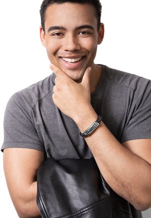Black leather jacket draped over arm, gray T-shirt, silver and black wrist bracelet, with a smiling young man touching his chin.