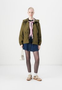 Olive green jacket with a hood over a light pink sweater, paired with a blue denim skirt, sheer tights, and patterned sneakers.