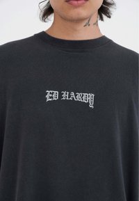 Camiseta de algodón negra con un logo bordado en blanco "ED HARDY" en el frontal. Cuello redondo, mangas cortas y textura suave.