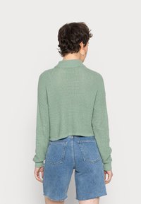 Ljusgrön, texturerad stickad tröja med krage, kort modell och långa ärmar, kombinerad med blå denimshorts med bakfickor.