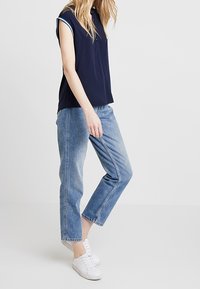 Polo navy a maniche corte con colletto, abbinato a jeans dritti azzurri e sneaker bianche. Tessuto morbido con vestibilità rilassata.