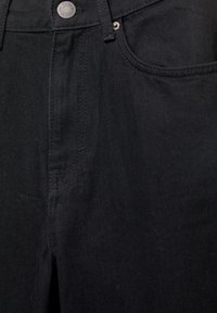 Jean en denim noir avec un design classique à cinq poches, une fermeture à bouton argenté et des détails de couture subtils sur un tissu texturé.