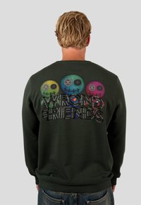 Sudadera verde oscuro con gráficos de calaveras coloridos y el texto "WRONG FRIENDS" en letras grandes, con puños y dobladillo acanalados.