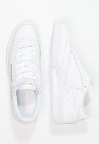 Valkoiset nahkakengät Reebok, joissa on rei'itetty kärki, nauhakiinnitys ja teksturoitu kumipohja, jossa on minimaalista brändäystä.