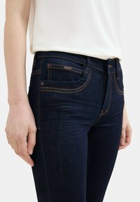 Jeans ajustados de denim azul oscuro con costuras de contraste en naranja, diseño de cinco bolsillos y cierre de botón en la cintura.