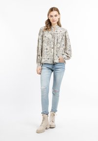 Hämodriger Bluse mit floralem Muster in Creme mit Puffärmeln und Schleifenkragen. Getragen mit ausgebleichten hellblauen Jeans und beigen Schnürstiefeln.