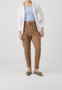 Hnědé cargo kalhoty se bočními kapsami, v kombinaci se světle modrým žebrovaným topem a bílou košili na knoflíky. Doplňují je hnědé espadrilky.