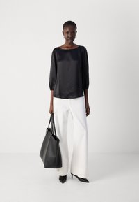 Zwarte satijnen blouse met pofmouwen, gedragen met witte wijde broek, zwarte puntige hakken en een grote zwarte schoudertas.